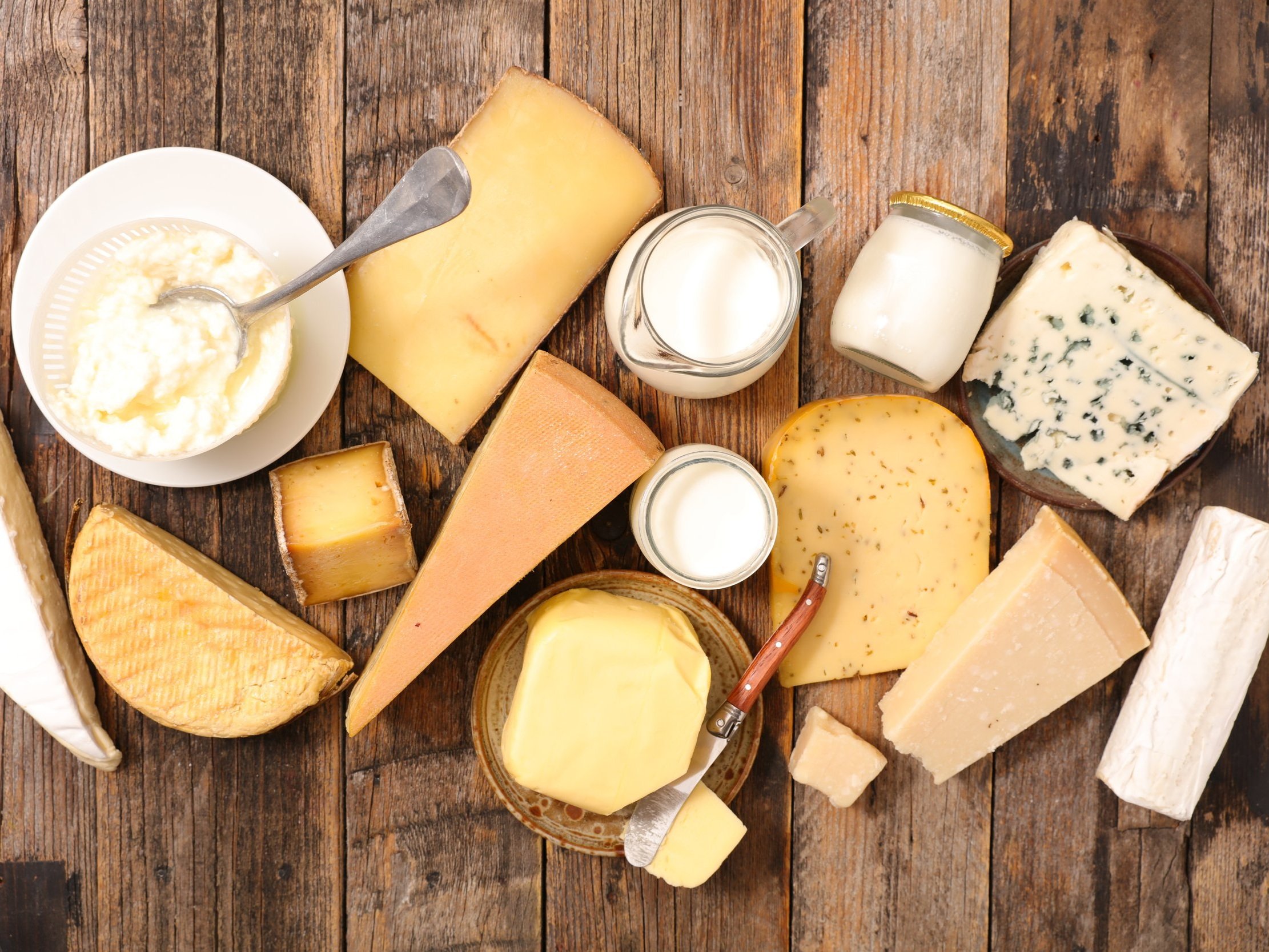 cheese_assorted1 (1) An assortment of various cheeses including soft, hard, and blue cheeses, along with bowls of cream and milk, arranged on a rustic wooden surface.