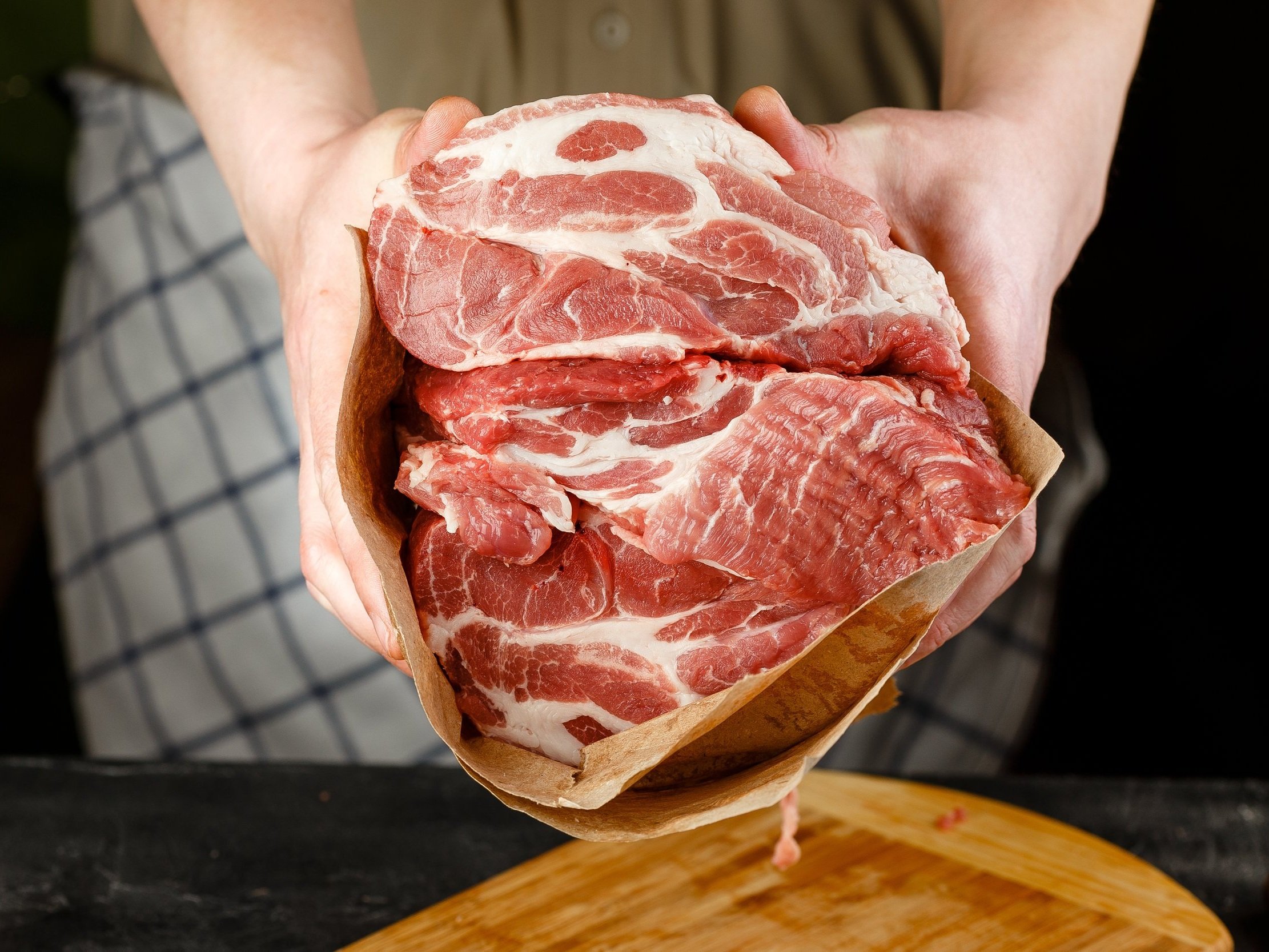 pork_shoulder_raw (4) Close-up of hands holding a package of fresh, marbled pork meat, showcasing its rich red color and fat layers, ideal for cooking and grilling.